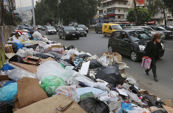 In this Thursday, Dec. 17, 2015 photo, a Lebanese woman covers her nose from the smell as she passes by a pile of garbage on a street in Beirut, Lebanon. Lebanon’s trash collection crisis which set off summer protests is entering its sixth month, but you would hardly be able to know it in Beirut. (AP Photo/Bilal Hussein) ORG XMIT: XBH506